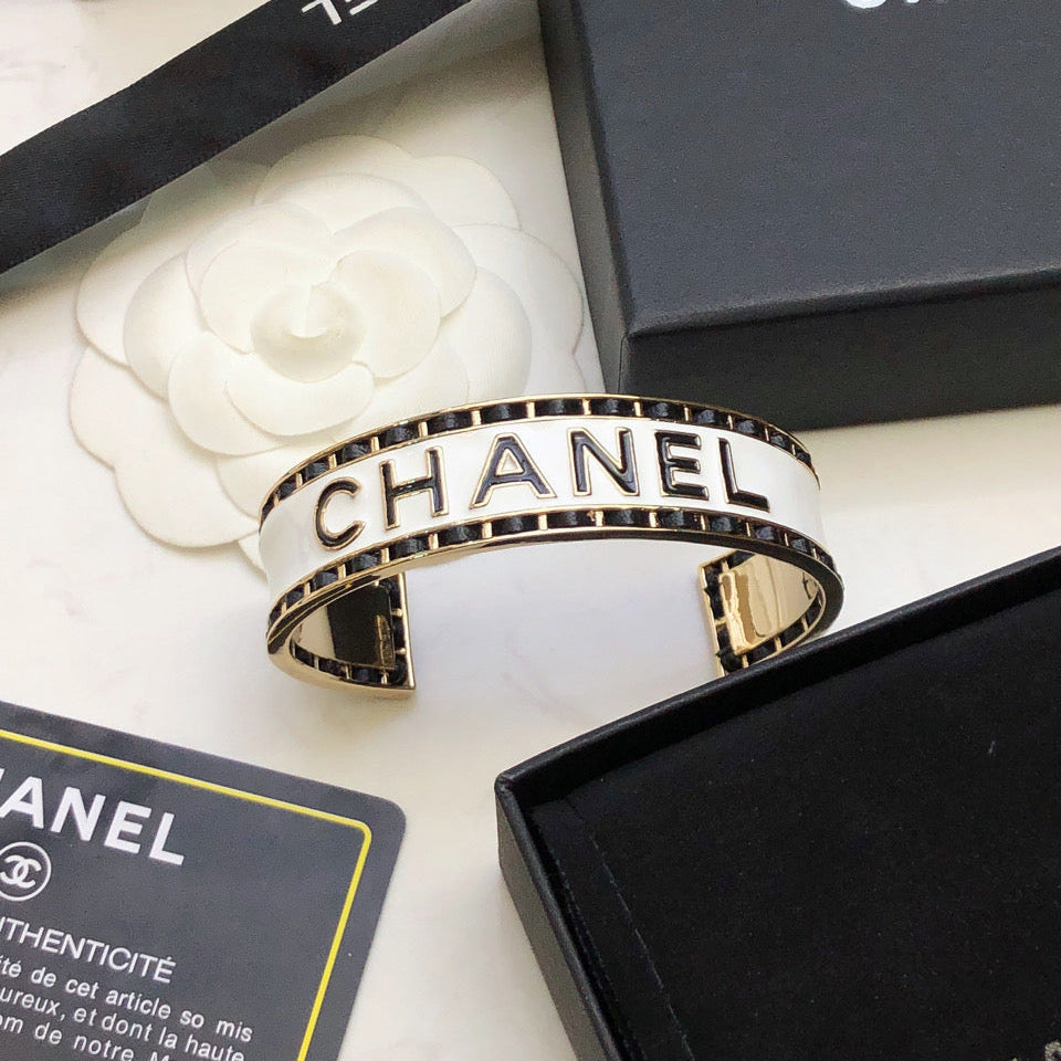 CHANEL 26S CHANEL LOGO ENAMEL CUFF BRACELET WITH BLACK TRIM IN GOLD METAL 630835