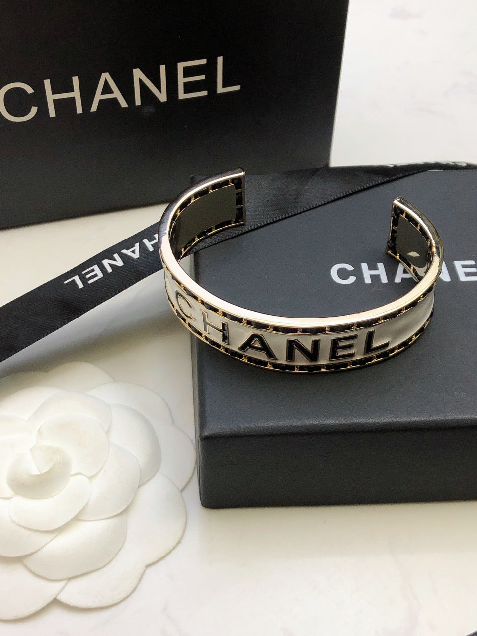 CHANEL 26S CHANEL LOGO ENAMEL CUFF BRACELET WITH BLACK TRIM IN GOLD METAL 630835